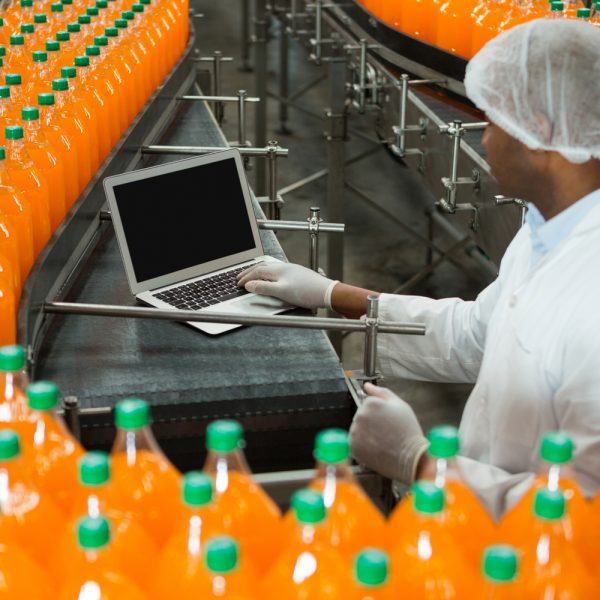 High angle view of male worker using laptop amidst production line in juice factory