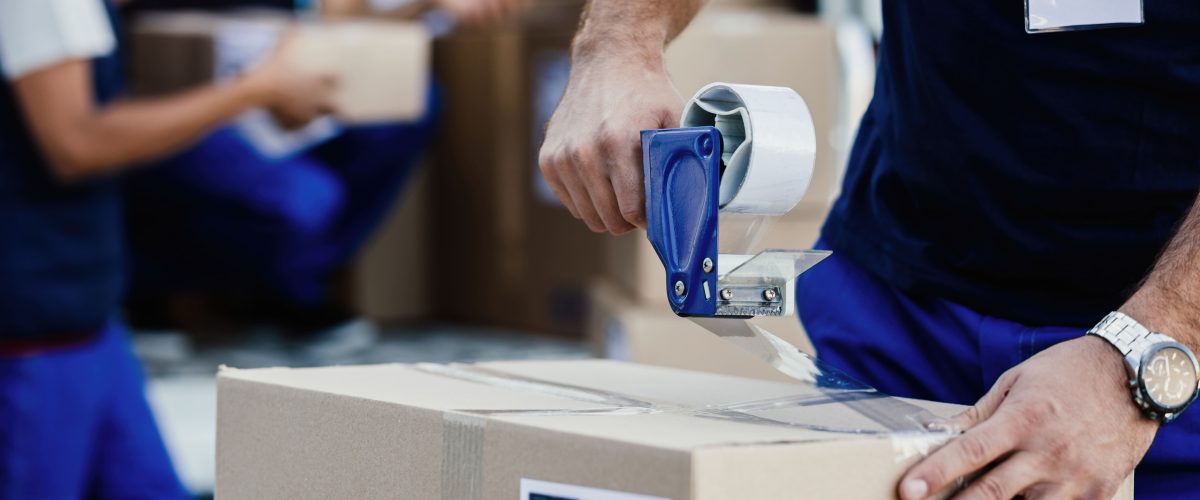 closeup-delivery-man-closing-carboard-box-with-tape-while-preparing-packages-shipment